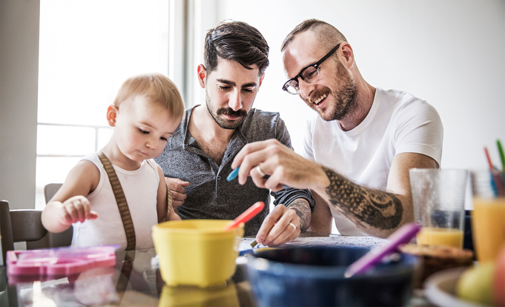 Two white males are sitting together doing arts and crafts with their toddler